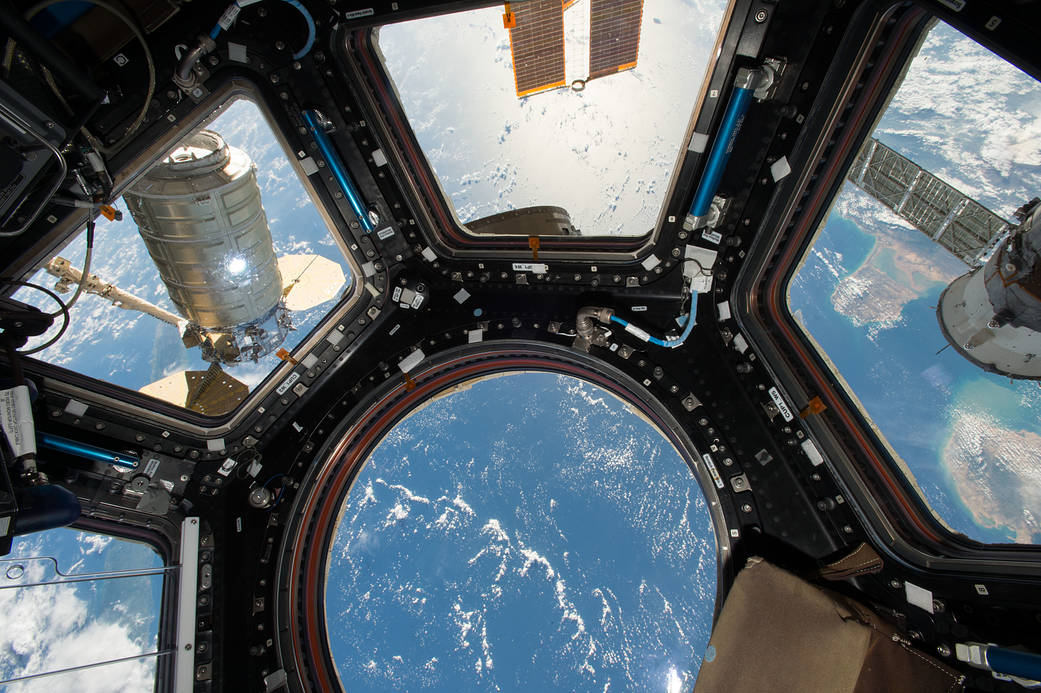 Orbital ATK's Cygnus cargo craft (left) is seen from the Cupola module windows aboard the International Space Station on Oct. 23, 2016. The main robotic work station for controlling the Canadarm2 robotic arm is located inside the Cupola and was used to capture Cygnus upon its arrival. The Expedition 49 crew will unload approximately 5,000 pounds of science investigations, food and supplies from the newly arrived spacecraft.