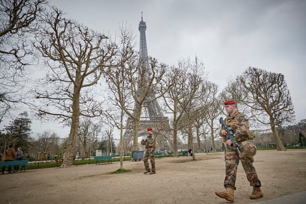 French army soldiers are walking in the park around the Eiffel Tower.
