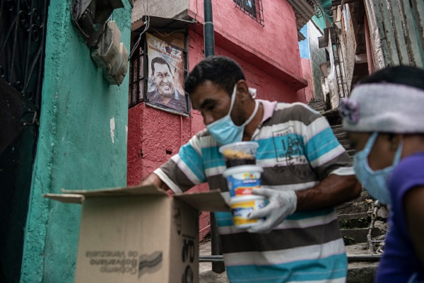 A man wearing a protective mask delivers free food to the comunity as part of the goverment initiative in front of a poster of late President Hugo Chavez in Petare on March 23, 2020 in Caracas, Venezuela.