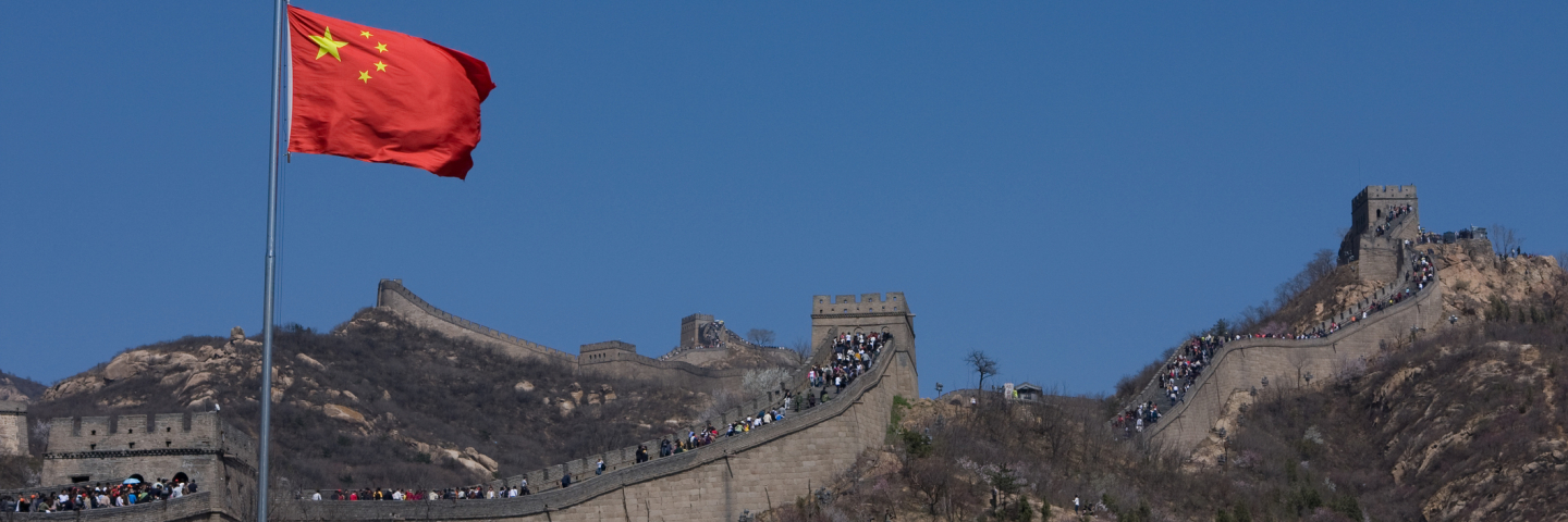 A photograph of the Great Wall China with the Chinese flag waving in the wind.