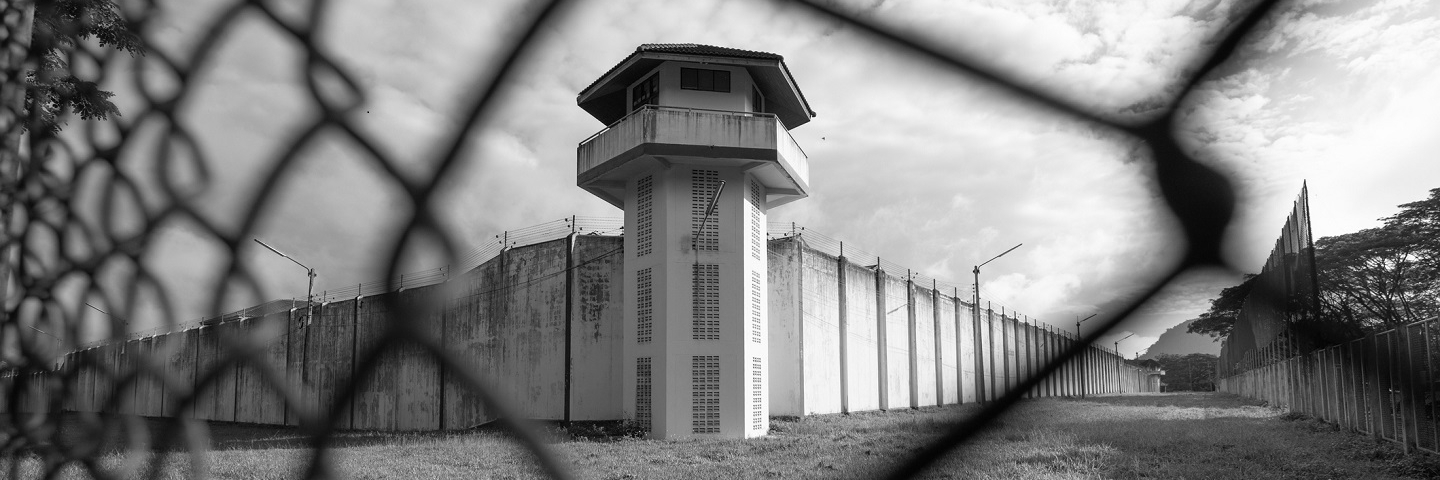 Prison watchtower protected by wire of prison fence.White prison wall and guard tower with coiled barbed wire.