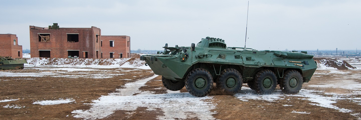 Photograph of a vehicle training for urban warfare in an abandoned field wiht empty apartment complexs in the background.