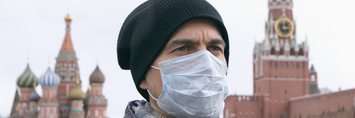 Portrait of adult man with medical protective mask on face with Kremlin and Red square on background.