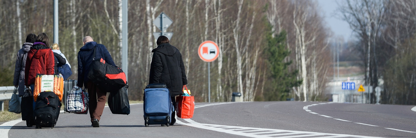 A photograph of Ukrainian citizens carry their belongings as they walk towards a border check point to take an Ukrainian bus at the Polish-Ukrainian border Korczowa on March 28, 2020 in Korczowa, Poland.