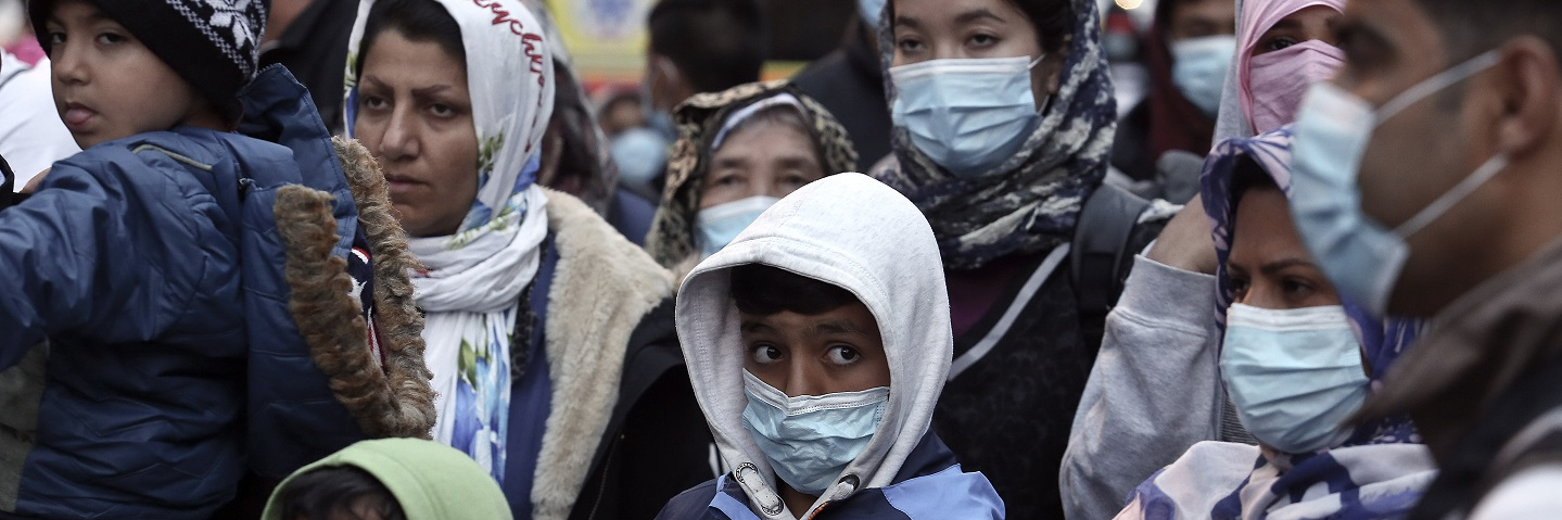 Migrants from the Moria camp in Lesbos island wearing masks to prevent the spread of the coronavirus, wait for a bus after their arrival at the port of Piraeus on May 4, 2020 in Athens, Greece.