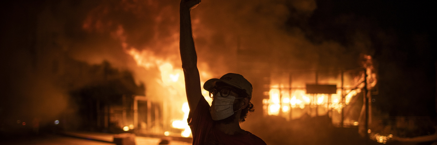 A protester wearing a face mask raises his fist in front of a burning building as large-scale protests resume on June 11, 2020 in Beirut, Lebanon.