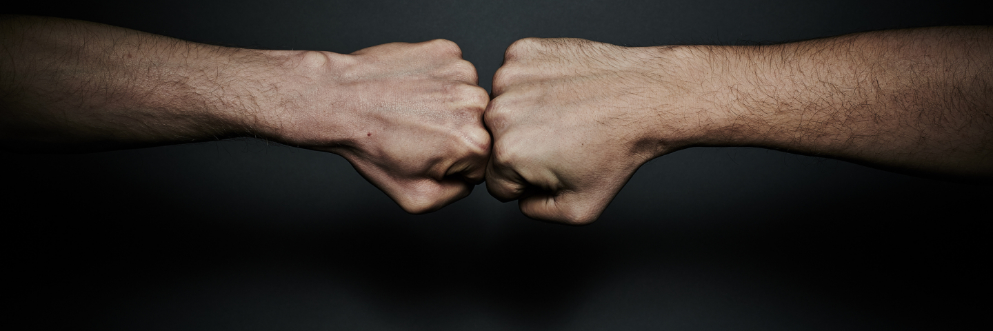 Two male fists in confrontation, placed one to the other. Hands are tensed.