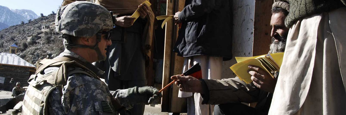 A soldiers from the 324th Psychological Operations Company, 14th Psychological Operations Battalion, Joint Psychological Task Force hands out flags and stickers to the people of Naray, Konar province.