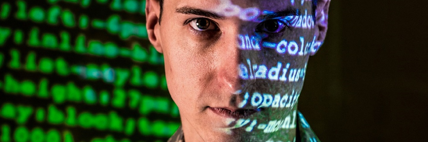 Close up of an Air Force cyber warfare specialist with code in the background and reflecting on his face.