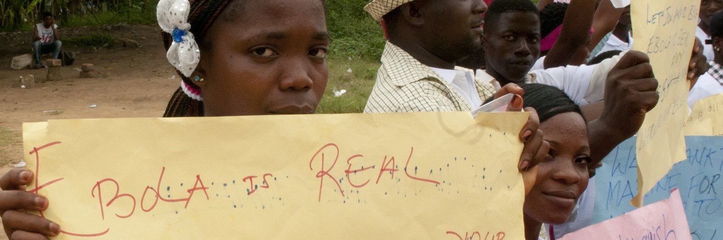 A girl in Liberia holds a sign that reads, "Ebola is real. Please listen to your authority, keep washing your hands."