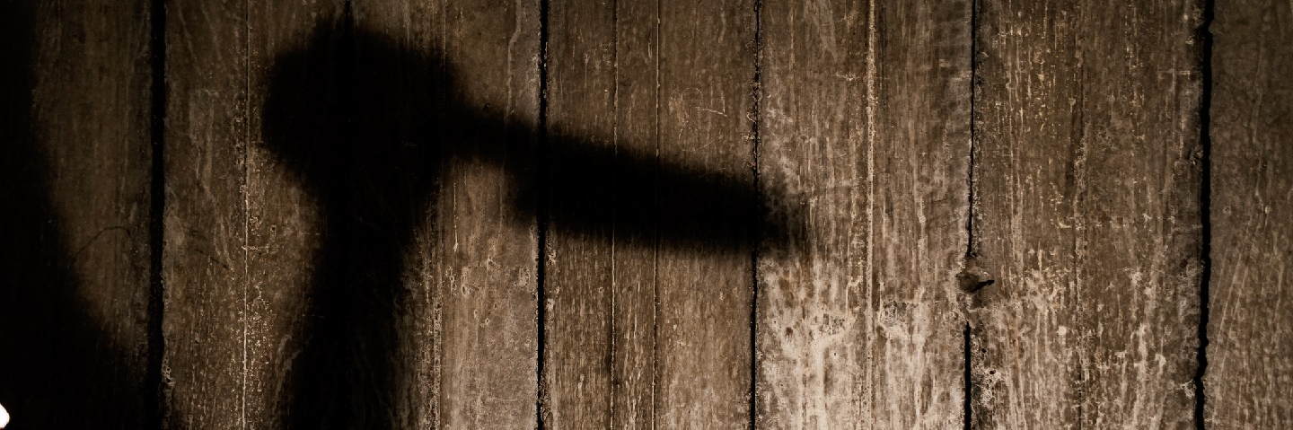 Shadow of an arm holding a knife in front of a wooden wall