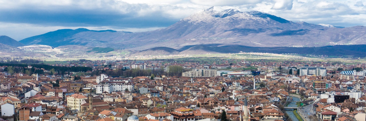 Photo of Kosovo, including city, mountains in the background and a river.