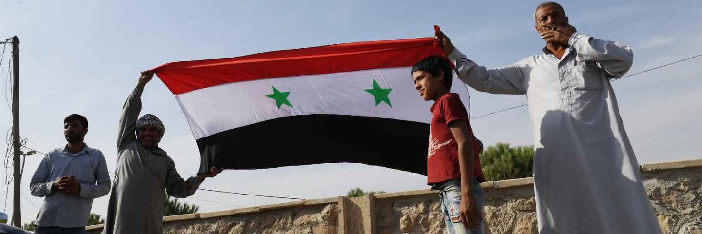 Locals hold the Syrian national flag in the village of al-Sultaniyah on the outskirts of the town of Manbij, which is now controlled by Syrian regime forces, on October 15, 2019.