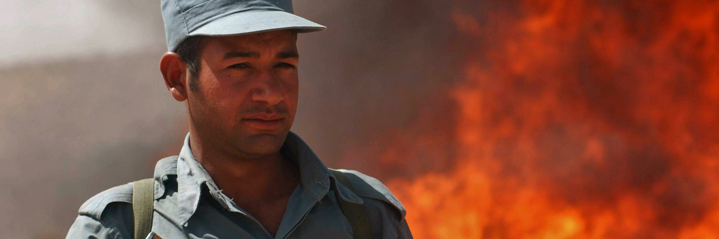 An Afghan policeman stands guard as officials in Herat province burn a pile of opium
