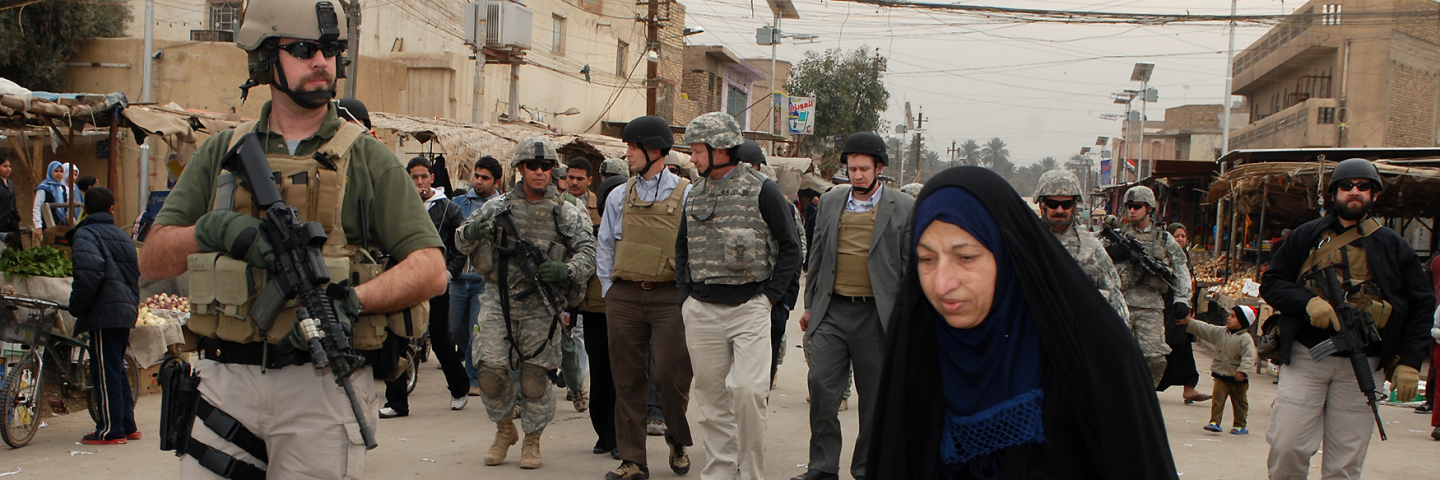 An Iraqi woman walks her produce-filled wheel barrel across the street in front of delegates from the House Appropriations Committee for Foreign Operations as they walk through the "fish market" in the Shababkhar neighborhood.