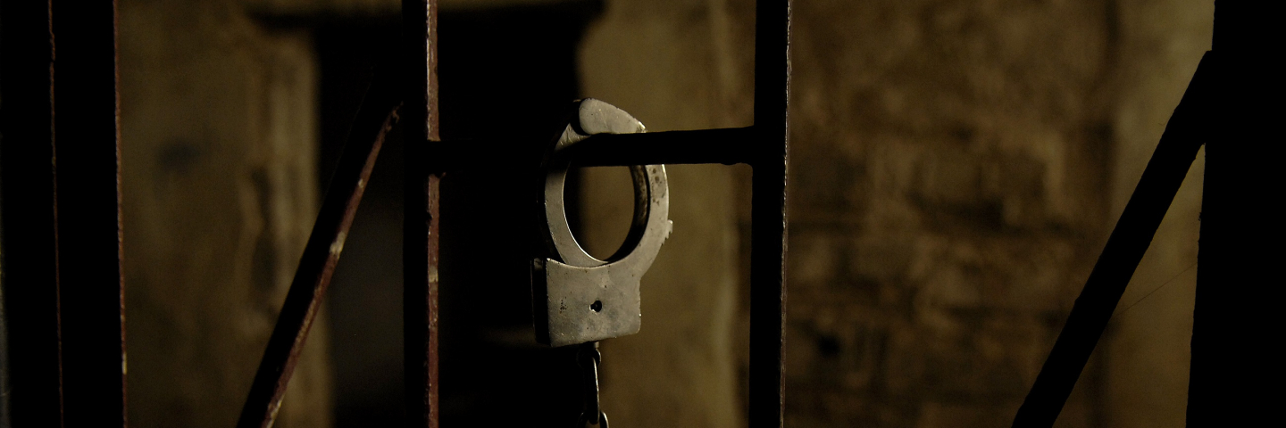 A handcuff hanging from a bar in a prison cell.