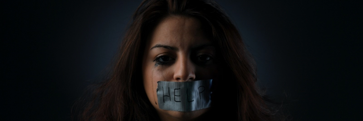 Photograph of a women with duct tape over her mouth with the "help" written on it.
