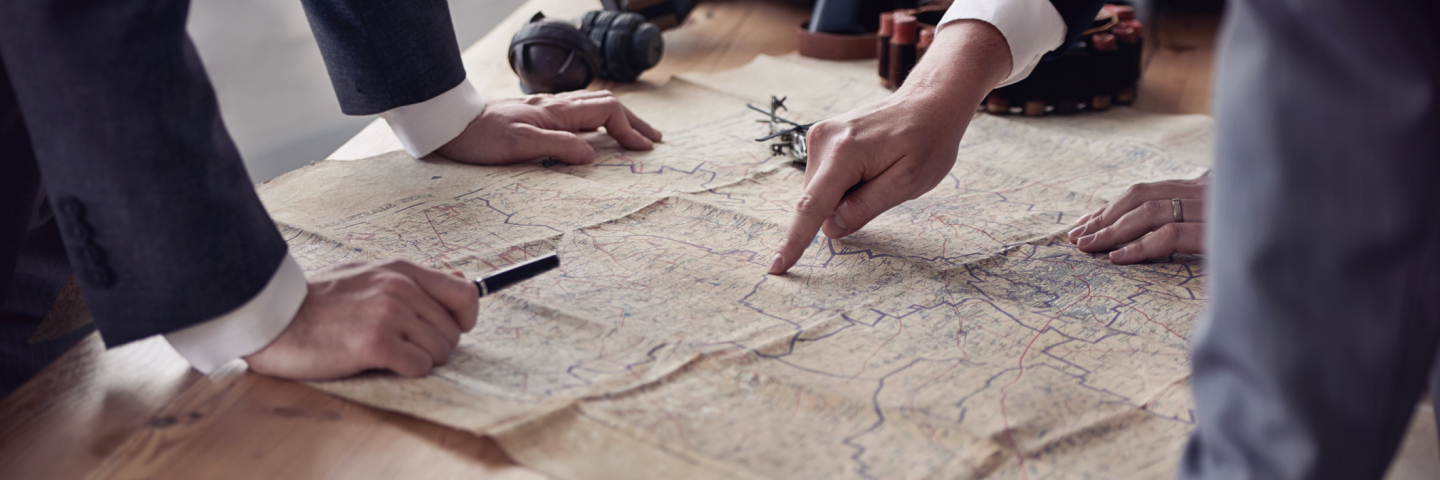 The hands of three men in suits discussing plans while looking at a map lying on a table