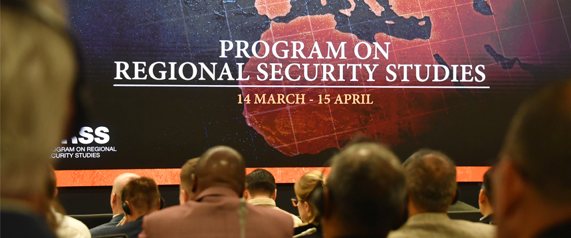Attendees seated in an auditorium view a large screen displaying “Program on Regional Security Studies, 14 March – 15 April,” with a stylized map of Europe and surrounding regions marked with flag icons, including NATO, EU, U.S., Russia, and China.
