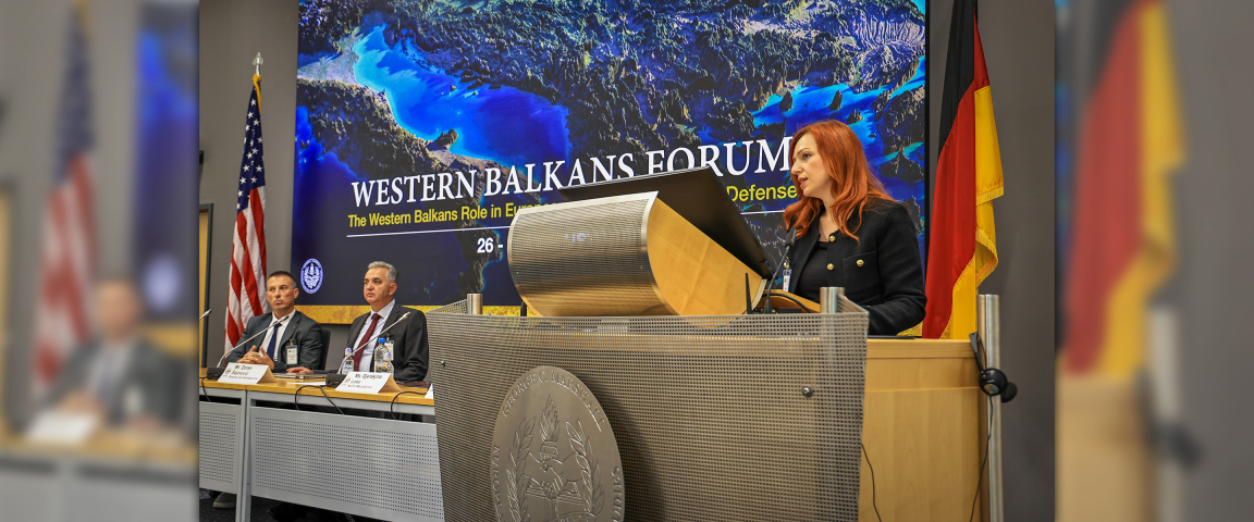 Gjeraqina Leka, assistant professor at the University of Tetova, speaks at the podium during the Western Balkans Forum at the Marshall Center in Garmisch-Partenkirchen, Germany. Behind her, a screen displays the event title alongside the U.S. and German flags. Three panelists are seated at the table to her left.