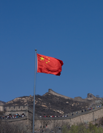 A photograph of the Great Wall China with the Chinese flag waving in the wind.