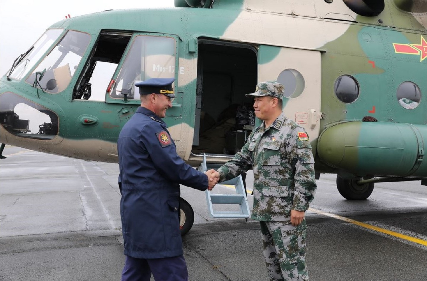 A Russian and a Chinese officer are shaking hands in front of a Chinese helicopter.