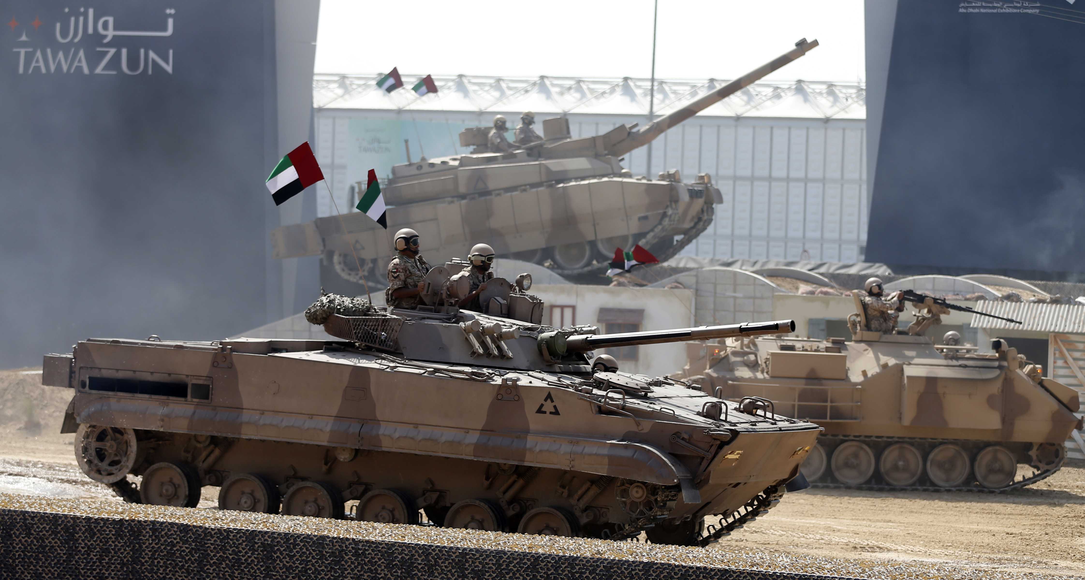 A tank driving down the road surrounded with two other tanks in the background.