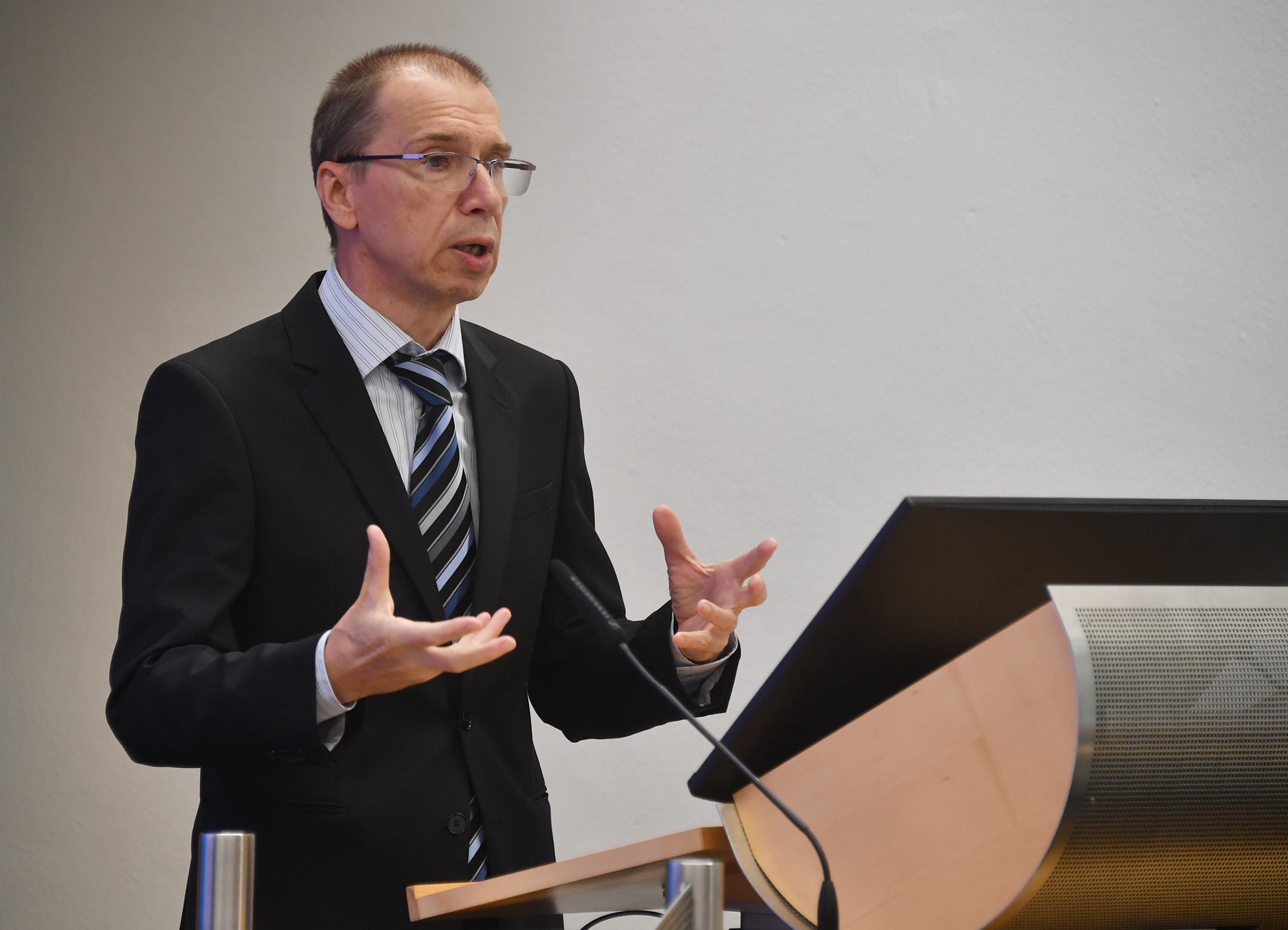 Vitalie Armașu speaks at a podium during his alumni scholar presentation at the Marshall Center, gesturing with both hands while addressing the audience.