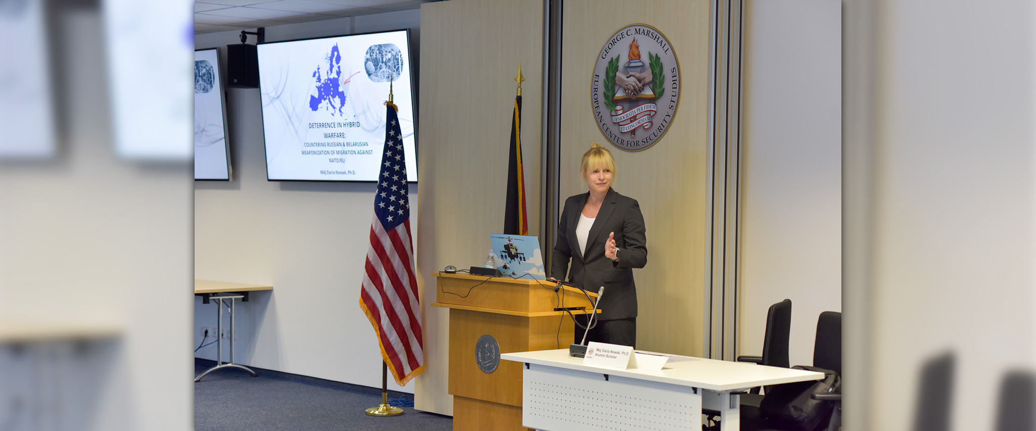 Blonde woman speaks behind a podium with US and German flag behind her. 
