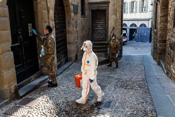 Two members of the military order of the Italian Red Cross escort in an alley of the old city, a member of the Italian Red Cross during his round of visits to the home of COVID-19 positive patients on April 6, 2020 in Bergamo, Italy.