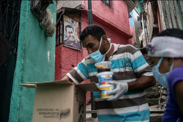 A man wearing a protective mask delivers free food to the comunity as part of the goverment initiative in front of a poster of late President Hugo Chavez in Petare on March 23, 2020 in Caracas, Venezuela.