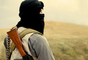 Hooded militant holding a weapon looking into the distance.