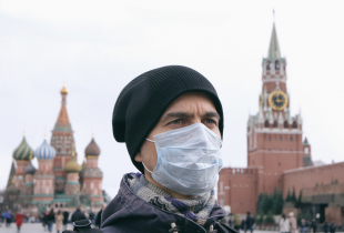 Portrait of adult man with medical protective mask on face with Kremlin and Red square on background.