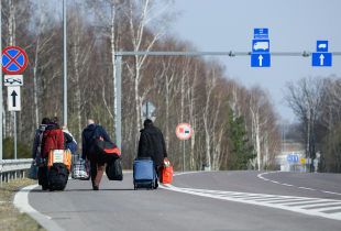 A photograph of  Ukrainian citizens carry their belongings as they walk towards a border check point to take an Ukrainian bus at the Polish-Ukrainian border Korczowa on March 28, 2020 in Korczowa, Poland.