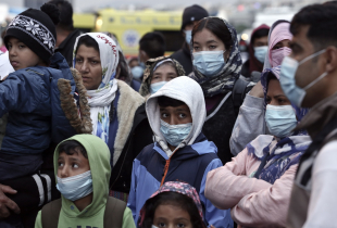 Migrants from the Moria camp in Lesbos island wearing masks to prevent the spread of the coronavirus, wait for a bus after their arrival at the port of Piraeus on May 4, 2020 in Athens, Greece.