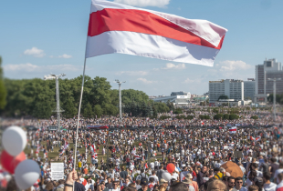 A photograph of a crowd of people with red and white balloons and flags.