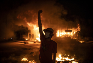  A protester wearing a face mask raises his fist in front of a burning building as large-scale protests resume on June 11, 2020 in Beirut, Lebanon.