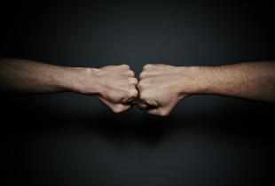 Two male fists in confrontation, placed one to the other. Hands are tensed.