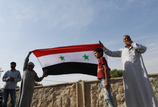 Locals hold the Syrian national flag in the village of al-Sultaniyah on the outskirts of the town of Manbij, which is now controlled by Syrian regime forces, on October 15, 2019.