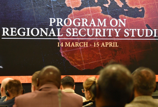 Attendees seated in an auditorium view a large screen displaying “Program on Regional Security Studies, 14 March – 15 April,” with a stylized map of Europe and surrounding regions marked with flag icons, including NATO, EU, U.S., Russia, and China.