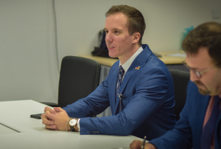 Two men in suits sit at a desk during a Marshall Center seminar. The man in the foreground, wearing a blue suit, speaks while seated, as the second man takes notes.