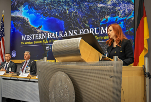 Gjeraqina Leka, assistant professor at the University of Tetova, speaks at the podium during the Western Balkans Forum at the Marshall Center in Garmisch-Partenkirchen, Germany. Behind her, a screen displays the event title alongside the U.S. and German flags. Three panelists are seated at the table to her left.
