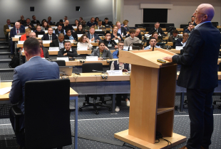Panelists addresses PASS participants from a podium during the afternoon session at the George C. Marshall Center. The audience of international security professionals sits in rows with laptops and nameplates visible.