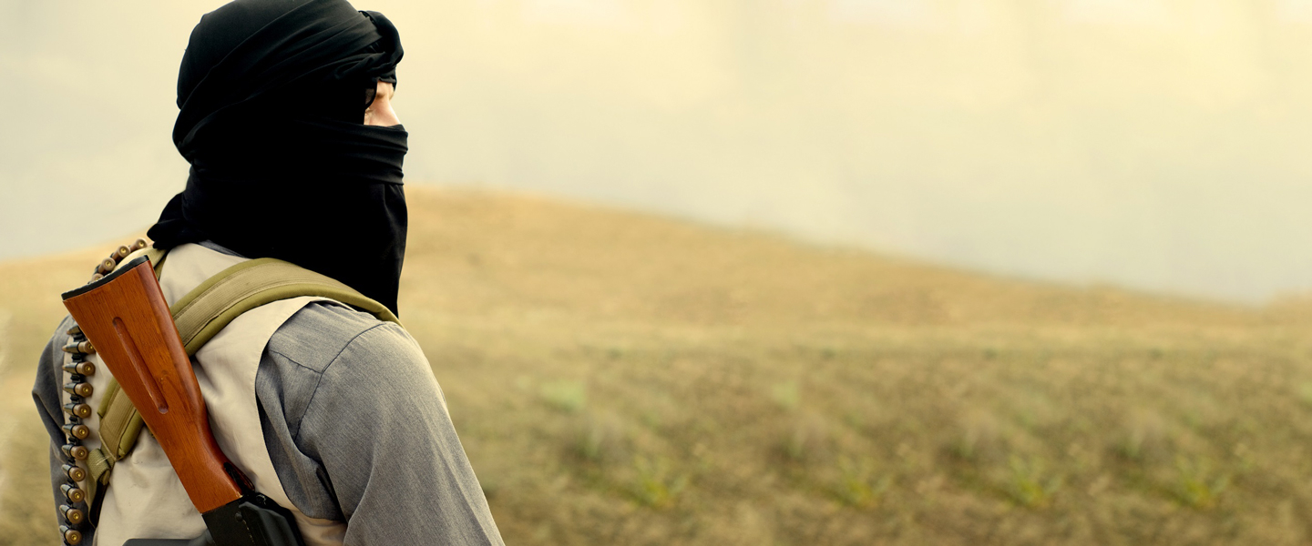 Hooded militant holding a weapon looking into the distance.