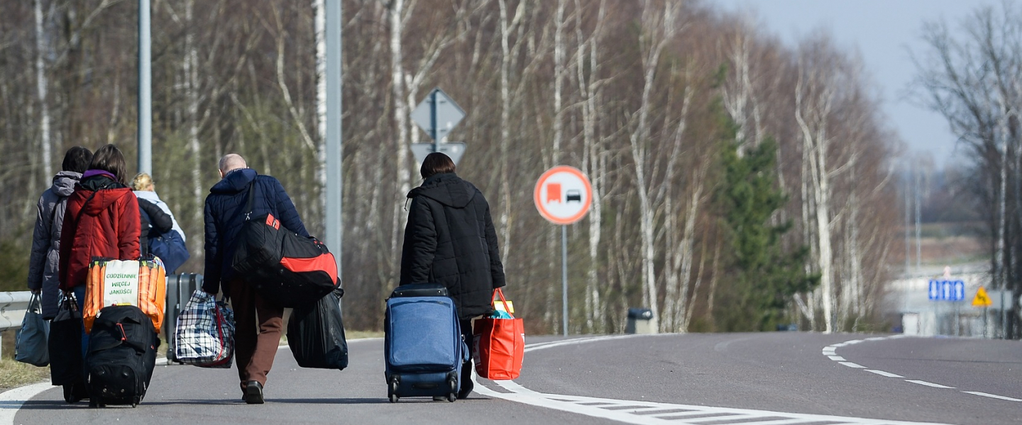 A photograph of  Ukrainian citizens carry their belongings as they walk towards a border check point to take an Ukrainian bus at the Polish-Ukrainian border Korczowa on March 28, 2020 in Korczowa, Poland.