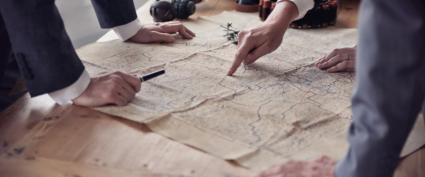 The hands of three men in suits discussing plans while looking at a map lying on a table