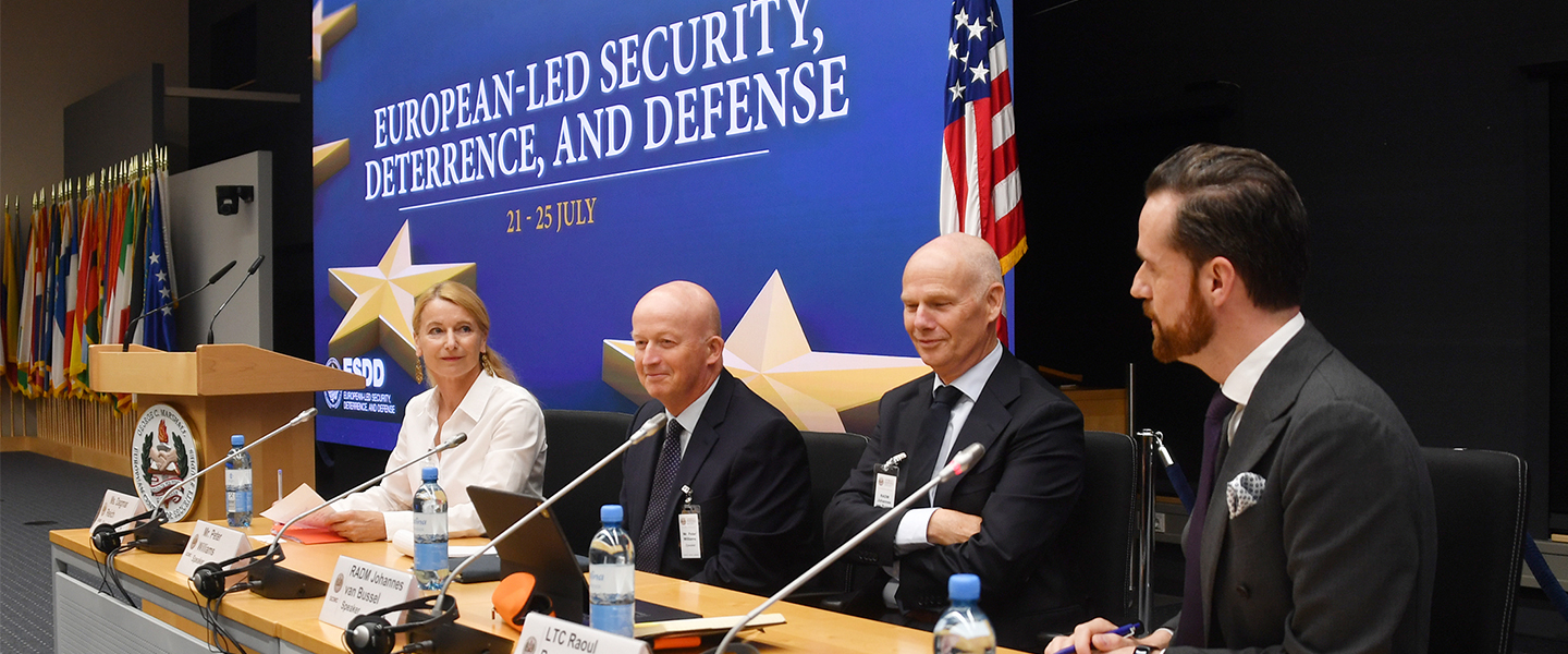Panelists seated at a conference table during the Seminar on European-Led Security, Deterrence, and Defense at the Marshall Center, with flags of NATO and partner nations in the background and the seminar title displayed on screen.